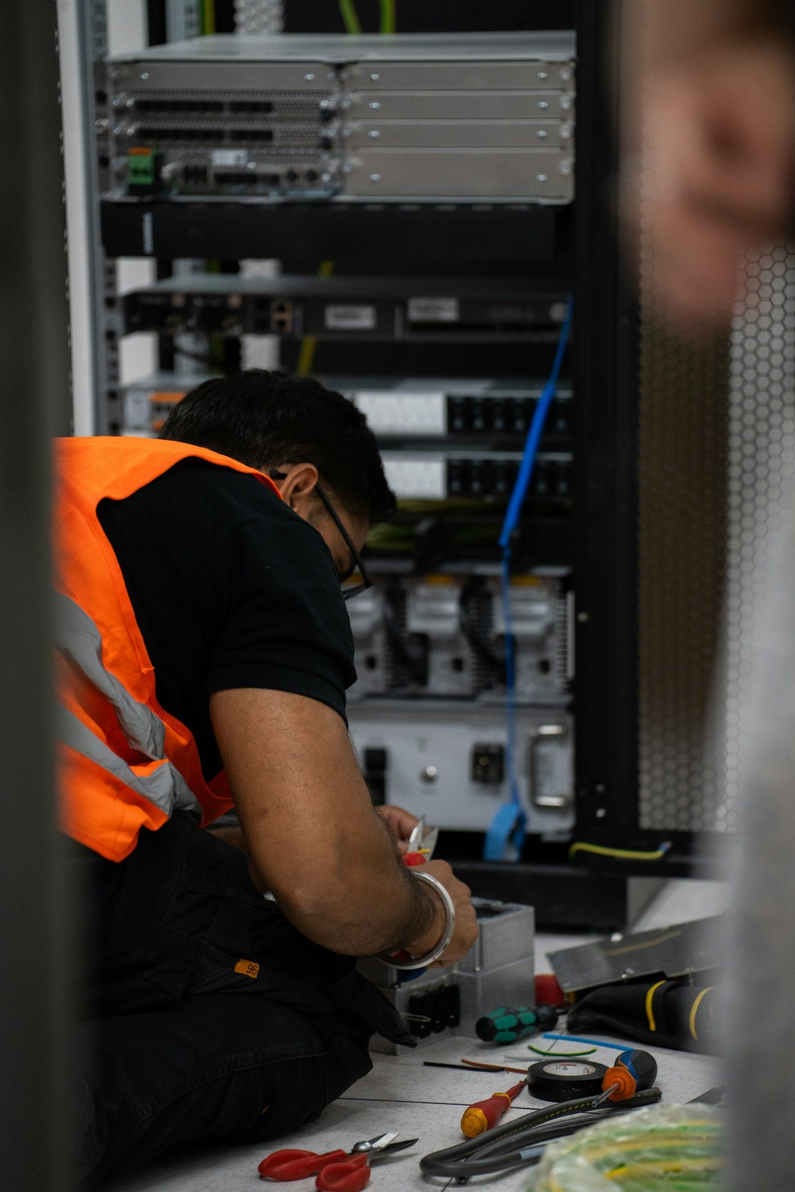 A technician in a safety vest working at an open network rack