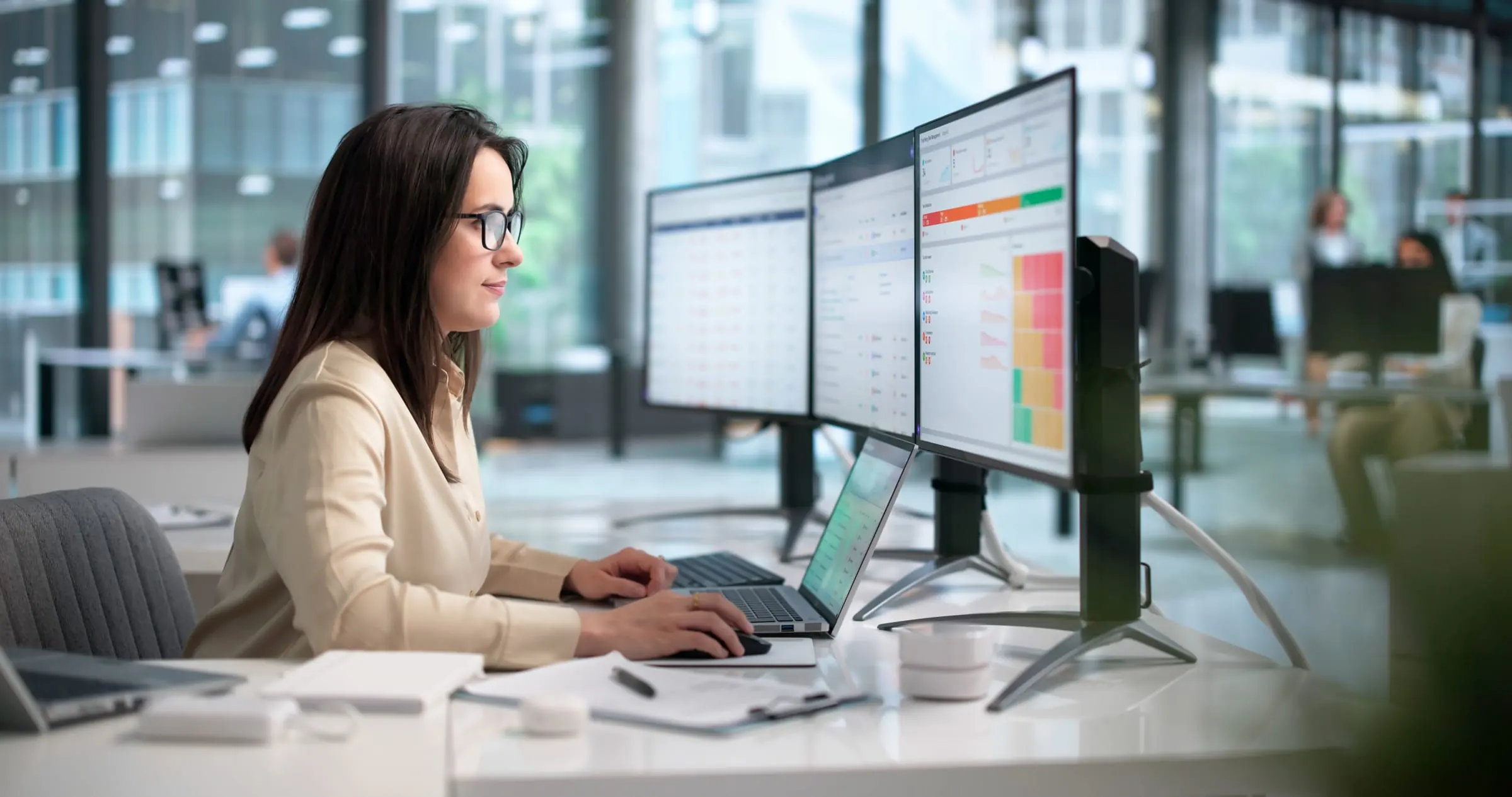 A professional working at a laptop and a row of monitors in an open office
